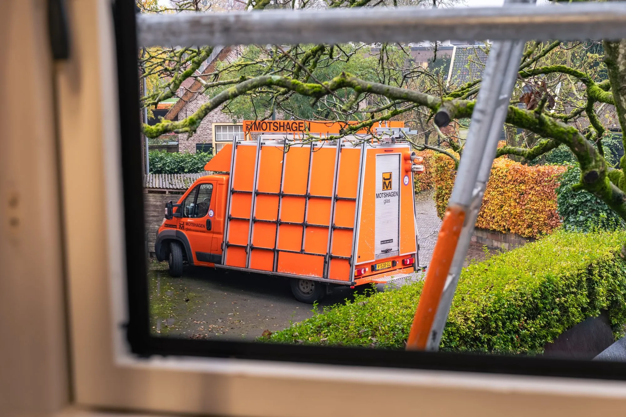 Oranje bedrijfsbus van Motshagen Glas, gezien door een raam